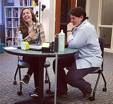 two young women at a round table, both laughing